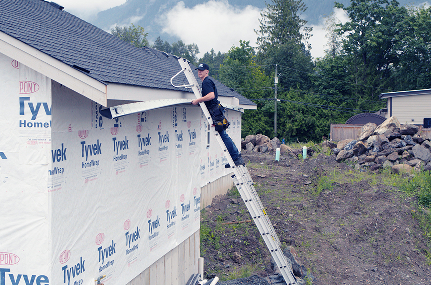 person installing gutter on side of building