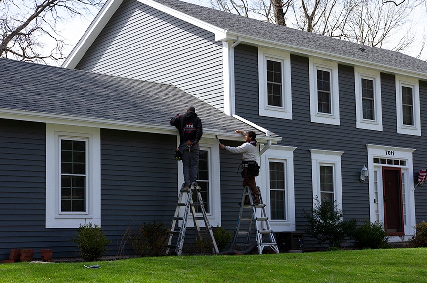 workers installing gutter on blue house