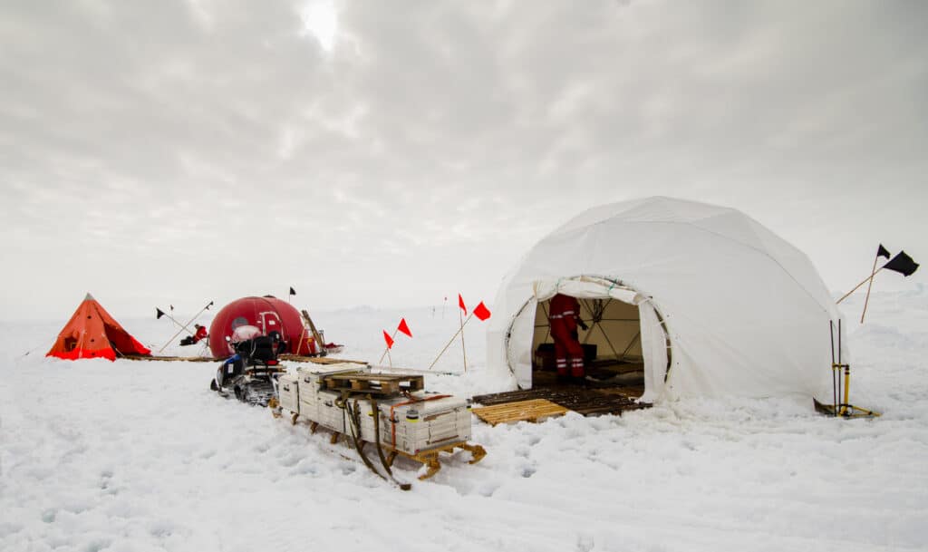 Job camp set up in Antartica with an igloo style tent and equipment on a sled.