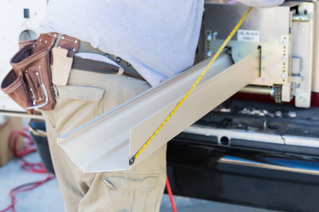 A worker measuring a gutter as its feeding out of a portable seamless gutter machine.