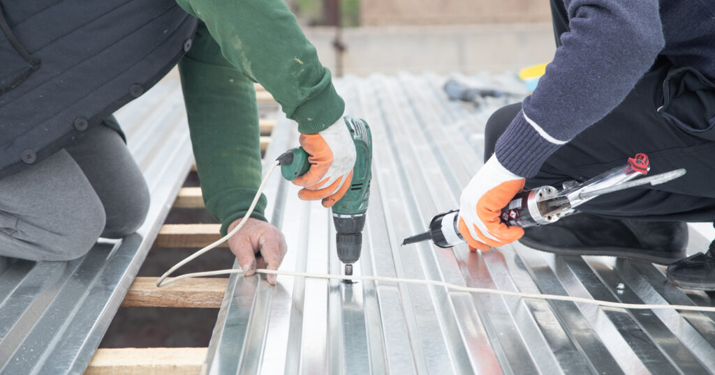 Man installing metal sheet roof with electric drill. 