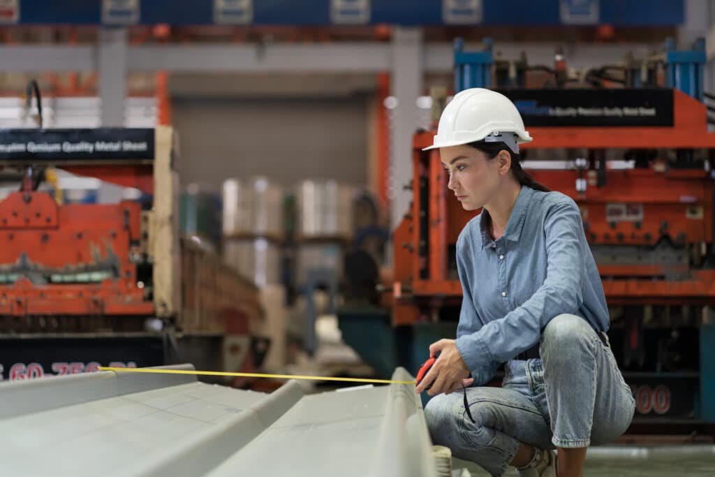 A woman measuring a metal panel in a factory.