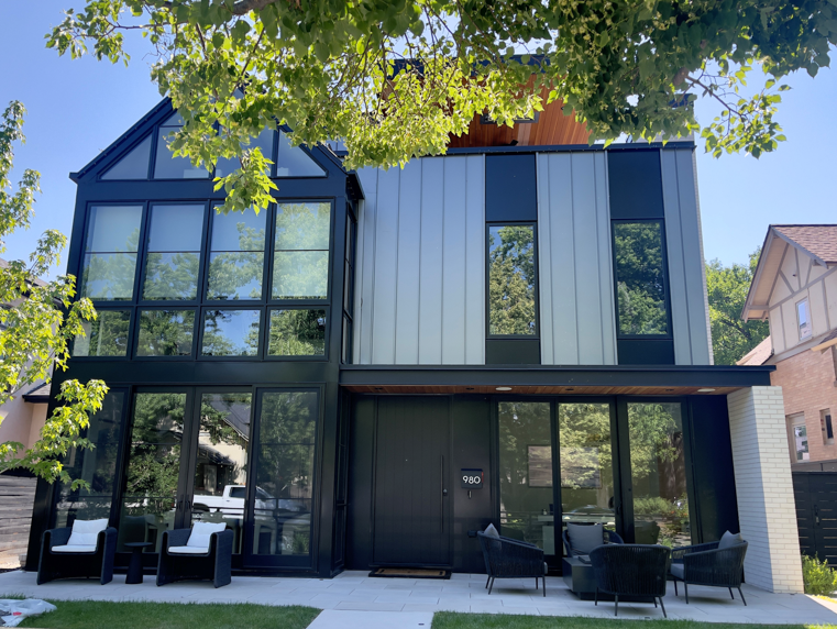 Modern Style black-and-white metal board and batten home with large windows and furnished front porch. 