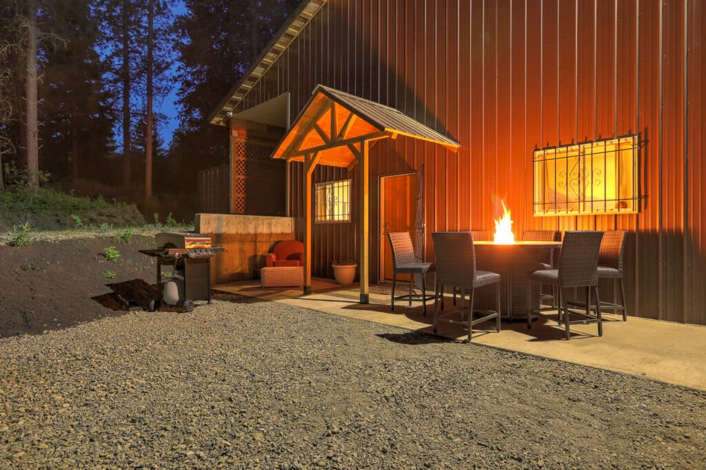 Front entrance to a barndominium with a firepit, surrounded by chairs, at night.