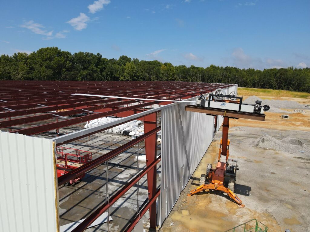 An NTM rollformer on a platform raised to roof level, fabricating a panel onto the roof frame.