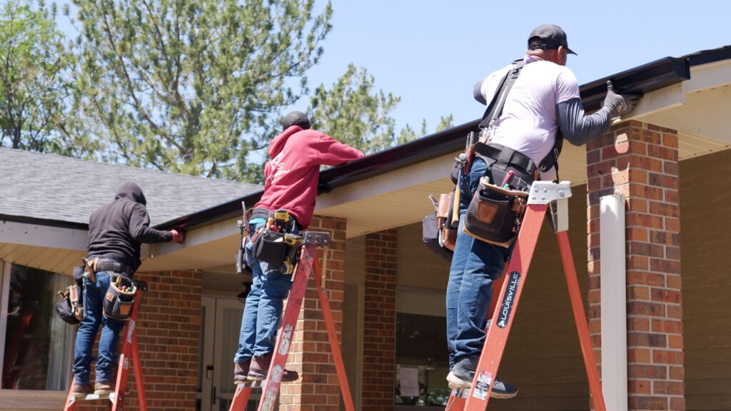 Three installers on ladders hanging seamless gutter on a residential roof