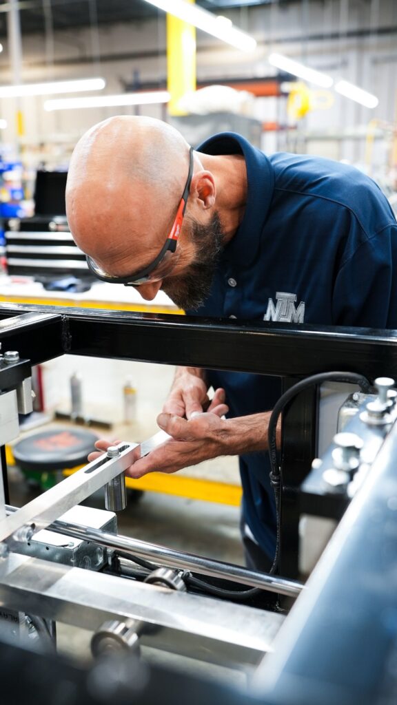 NTM production technician inspecting a rollforming machine on the Aurora shop floor.